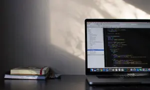 Laptop z kodem w edytorze, obok stos książek i ołówków.