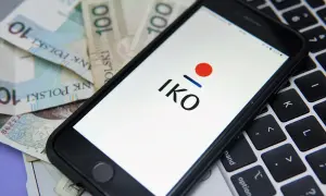 Chcesz wiedzieć, jak założyć IKO PKO? Na ekranie telefonu widzisz logo IKO, a obok polskie banknoty i klawiaturę laptopa.