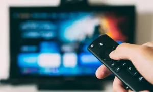 Ręka trzymająca pilot, ekran telewizora LG z kolorowymi ikonami. Dowiedz się, jak na telewizorze LG pobrać aplikacje.