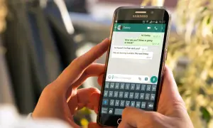 Dłonie trzymają smartfon z otwartym WhatsAppem. Widoczna jest klawiatura i okno czatu, co może pomóc w zrozumieniu, jak zainstalować WhatsApp.