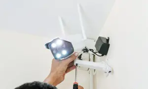 Montaż kamery zewnętrznej wifi. Ręka dokręca śrubę mocującą kamerę do uchwytu.