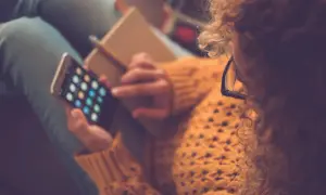 Kobieta z burzą loków i okularami na nosie przegląda aplikacje na telefonie, ucząc się, jak pobierać aplikacje na iPhone.