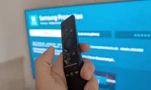 Pilot do telewizora Samsung w dłoni, ekran pokazuje menu, jak ściągnąć aplikacje na TV Samsung.
