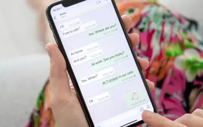 Dłoń trzyma smartfon z otwartym WhatsAppem, pokazującym rozmowę. To może być pomocne, gdy uczysz się, jak założyć WhatsApp krok po kroku.