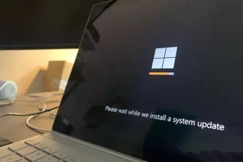 Ekran laptopa z logo Windows i komunikatem "Please wait while we install a system update". To ważny etap, jak aktualizować sterowniki, by system działał sprawnie.