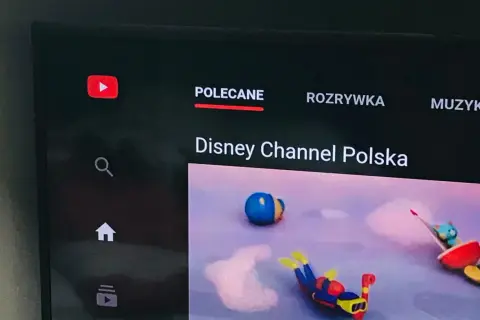 Ekran telewizora z aplikacją YouTube. Widoczne logo YouTube, menu "Polecane", "Rozrywka", "Muzyka" oraz kanał "Disney Channel Polska". Dowiedz się, jak zaktualizować aplikację YouTube.