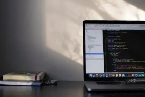 Laptop z kodem w edytorze, obok stos książek i ołówków.