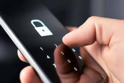 Dłoń wpisuje kod na ekranie telefonu, symbolizując jak zmienić kod w domofonie w bloku.