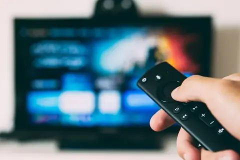 Ręka trzymająca pilot, ekran telewizora LG z kolorowymi ikonami. Dowiedz się, jak na telewizorze LG pobrać aplikacje.