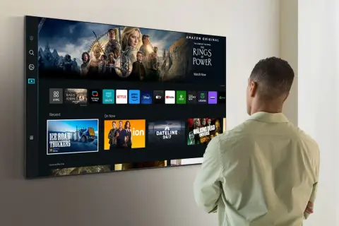 Mężczyzna patrzy na ekran telewizora Samsung Smart TV, gdzie wyświetlane są aplikacje i filmy. Dowiedz się, jak zaktualizować telewizor Samsung Smart TV, aby cieszyć się najnowszymi funkcjami.