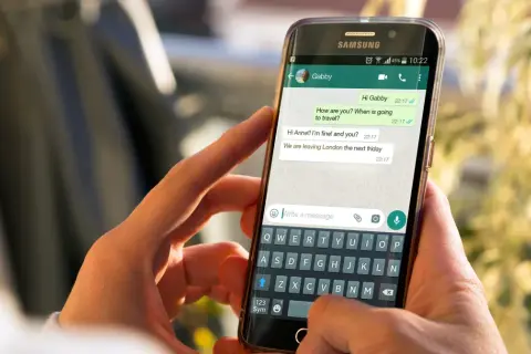 Dłonie trzymają smartfon z otwartym WhatsAppem. Widoczna jest klawiatura i okno czatu, co może pomóc w zrozumieniu, jak zainstalować WhatsApp.