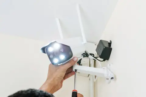 Montaż kamery zewnętrznej wifi. Ręka dokręca śrubę mocującą kamerę do uchwytu.