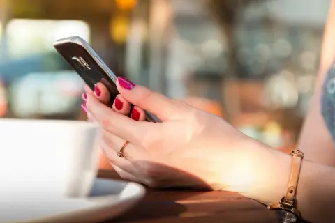 Kobieta z pomalowanymi paznokciami trzyma telefon, szukając informacji, jak zmienić dźwięk wiadomości w Messengerze.