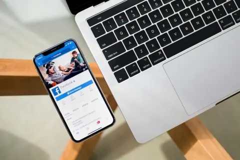 Chcesz wiedzieć, jak sprawdzić na jakich urządzeniach jesteś zalogowany na FB? Na ekranie telefonu widać stronę Facebooka, obok klawiatura laptopa.
