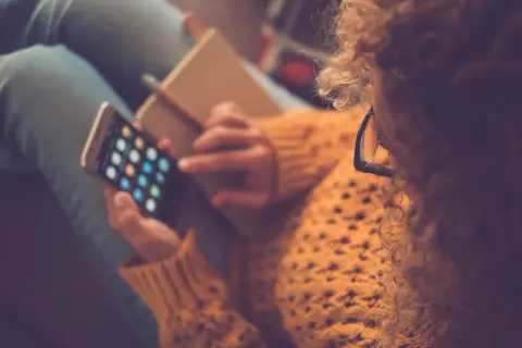 Kobieta z burzą loków i okularami na nosie przegląda aplikacje na telefonie, ucząc się, jak pobierać aplikacje na iPhone.