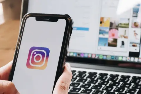 Telefon z logo Instagrama w dłoni, obok laptop z otwartą aplikacją. Dowiedz się, jak zmienić dźwięk powiadomień na Instagramie.