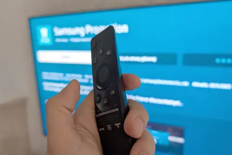 Pilot do telewizora Samsung w dłoni, ekran pokazuje menu, jak ściągnąć aplikacje na TV Samsung.