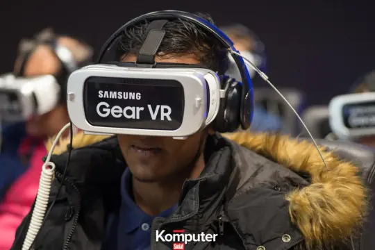 Osoba w goglach Samsung Gear VR, zastanawia się jakie gogle VR do telefonu wybrać. W tle inne osoby w podobnym sprzęcie.