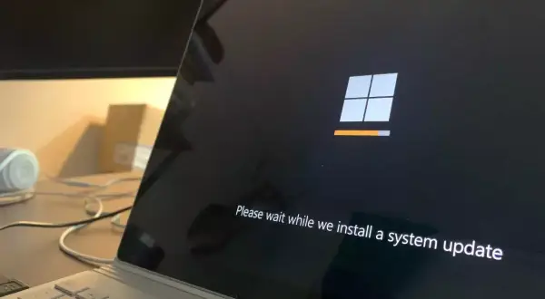 Ekran laptopa z logo Windows i komunikatem "Please wait while we install a system update". To ważny etap, jak aktualizować sterowniki, by system działał sprawnie.