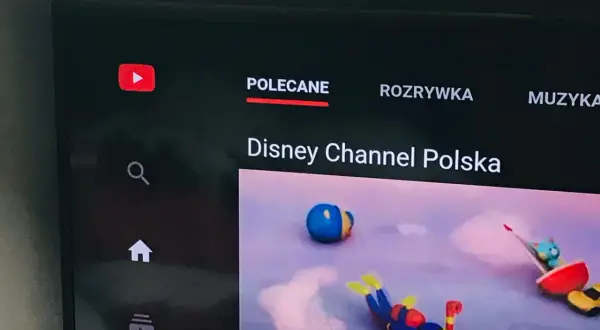 Ekran telewizora z aplikacją YouTube. Widoczne logo YouTube, menu "Polecane", "Rozrywka", "Muzyka" oraz kanał "Disney Channel Polska". Dowiedz się, jak zaktualizować aplikację YouTube.