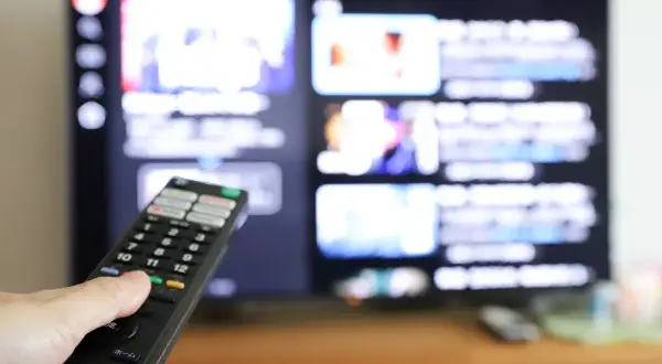 Dłoń z pilotem przed ekranem telewizora, na którym widać menu aplikacji. Dowiedz się, jak ściągnąć aplikację na telewizor.