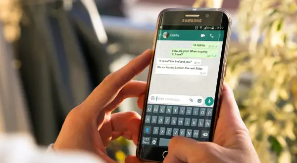 Dłonie trzymają smartfon z otwartym WhatsAppem. Widoczna jest klawiatura i okno czatu, co może pomóc w zrozumieniu, jak zainstalować WhatsApp.