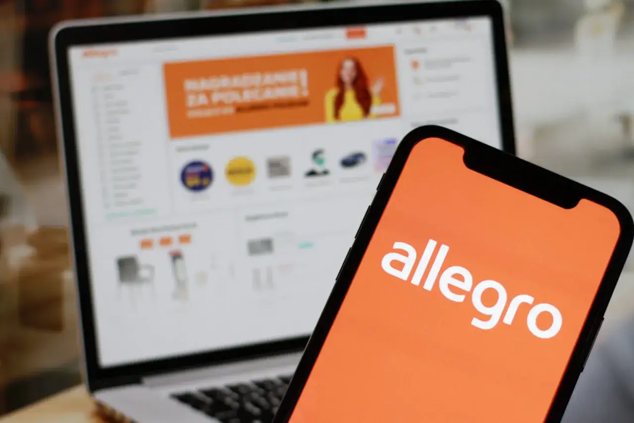 Aplikacja mobilna Allegro na ekranie smartfona obok laptopa z otwartą stroną Allegro.