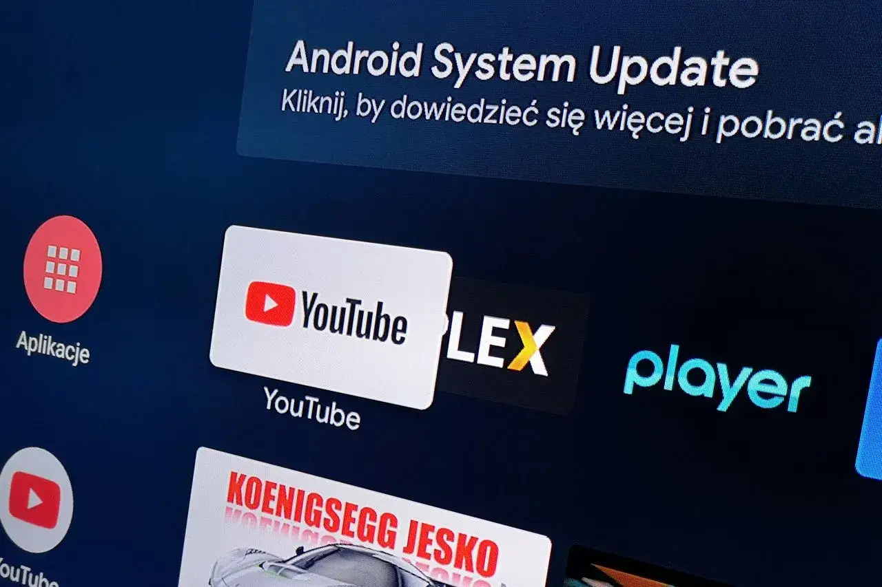 Ekran telewizora z aplikacjami: YouTube, Player, Plex. Widoczna też informacja o aktualizacji systemu Android. Chcesz wiedzieć, jak zaktualizować aplikację YouTube?