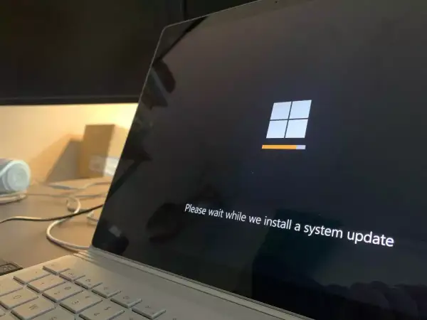 Ekran laptopa z logo Windows i komunikatem "Please wait while we install a system update". To ważny etap, jak aktualizować sterowniki, by system działał sprawnie.