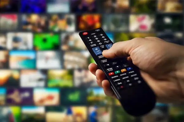 Dłoń trzymająca pilot do telewizora Samsung, gotowa do wykonania aktualizacji. Tło to mozaika ekranów.