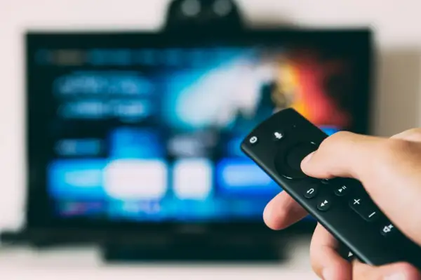 Ręka trzymająca pilot, ekran telewizora LG z kolorowymi ikonami. Dowiedz się, jak na telewizorze LG pobrać aplikacje.