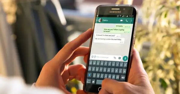 Dłonie trzymają smartfon z otwartym WhatsAppem. Widoczna jest klawiatura i okno czatu, co może pomóc w zrozumieniu, jak zainstalować WhatsApp.