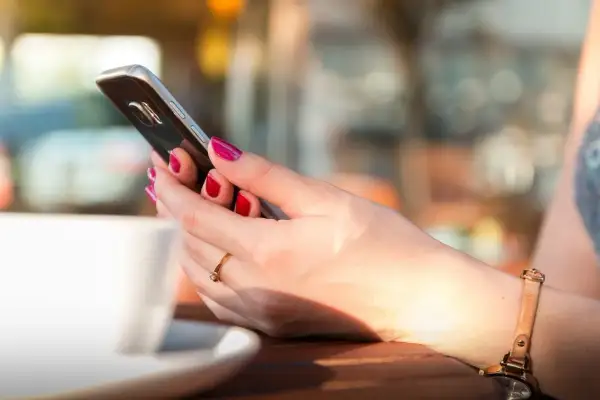 Kobieta z pomalowanymi paznokciami trzyma telefon, szukając informacji, jak zmienić dźwięk wiadomości w Messengerze.