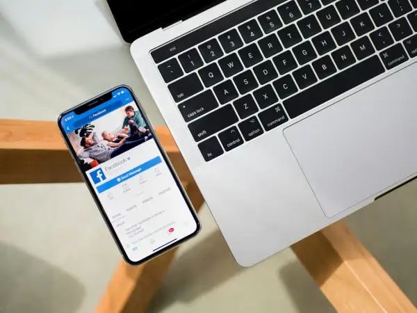 Chcesz wiedzieć, jak sprawdzić na jakich urządzeniach jesteś zalogowany na FB? Na ekranie telefonu widać stronę Facebooka, obok klawiatura laptopa.