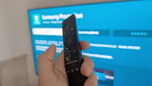 Pilot do telewizora Samsung w dłoni, ekran pokazuje menu, jak ściągnąć aplikacje na TV Samsung.